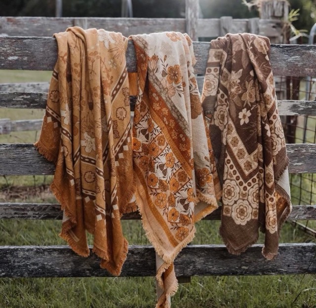 Handmade floral throw rugs draped over a timber fence