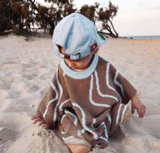 Child on the beach wearing a handmade knitted poncho